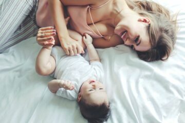 Moeder en baby liggen lachend op bed, moeder heeft grip op uitgaven door grip app