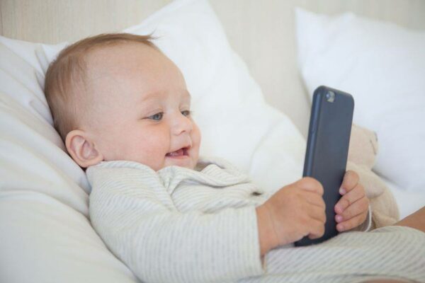 Baby ligt in bed met een smartphone