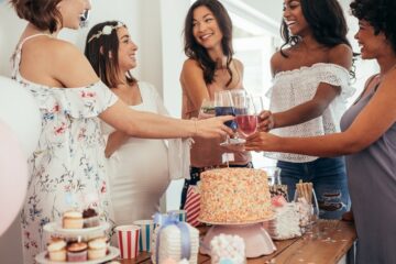 Zwangere vrouw en vriendinnen proosten rondom tafel met babyshowerhapjes en drankjes
