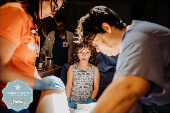 Meisje bekijkt verwondert naar het tafereel tussen haar moeders benen