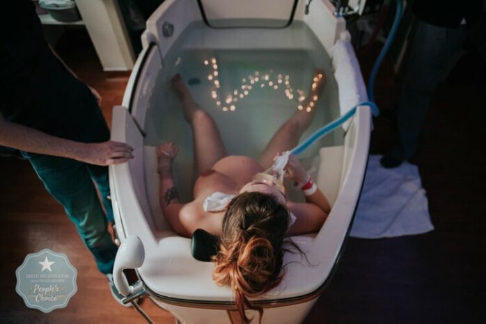 Vrouw is aan het bevallen in bad en neemt een lachgasmasker