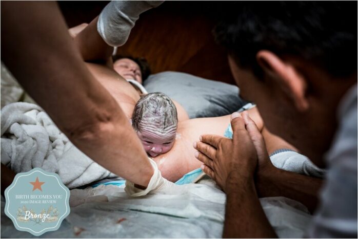 Vader bekijkt verwachtingsvol het hoofdje van de baby die al uit de vagina komt