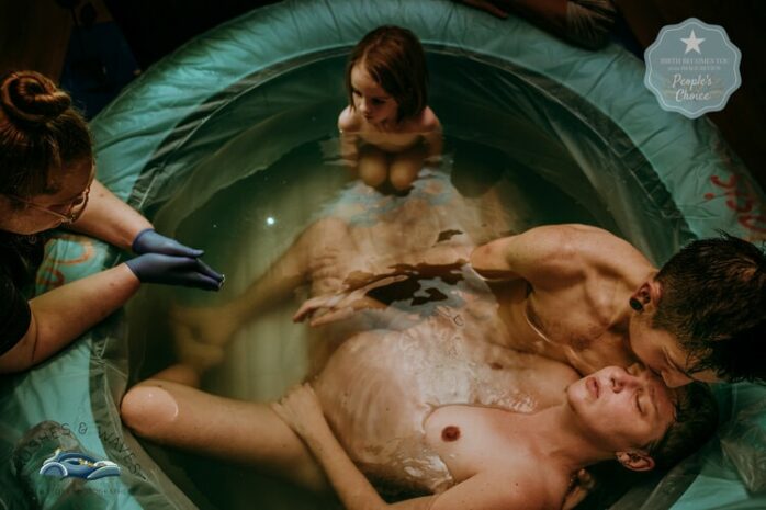 Partner en kleuter zitten bij moeder in bad die aan het bevallen is