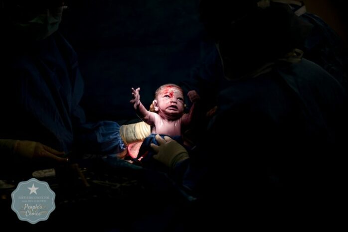 Pasgeboren baby staat in de spotlight en houdt zijn armen omhoog