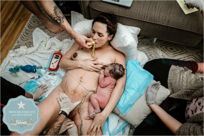 Vrouw ligt volledig uitgeput met haar pasgeboren baby in de armen en krijgt banaan gevoerd