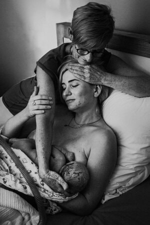 Moeder omhelst pas bevallen dochter die borstvoeding geeft aan baby