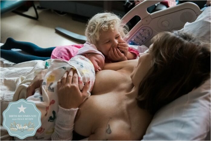 Peuter gniffelt terwijl haar moeder de newborn borstvoeding geeft