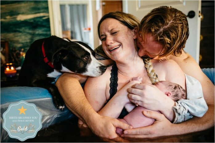 Ouders houden geëmotioneerd hun baby vast terwijl de hond ook komt kijken