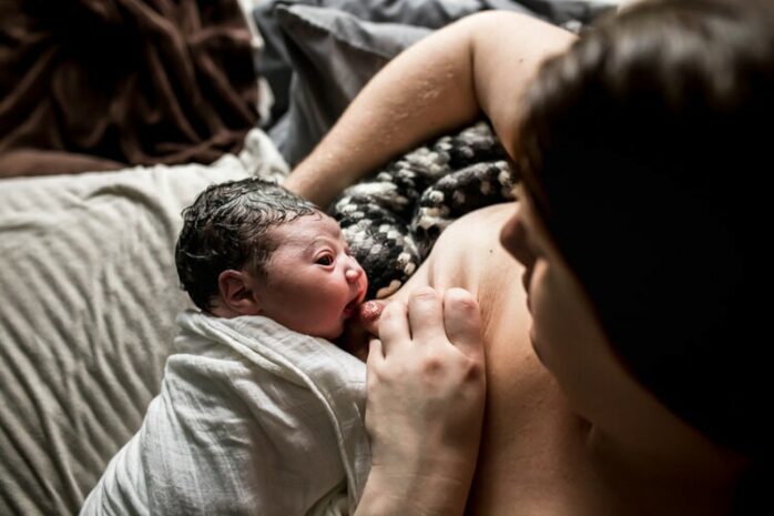 Vrouw legt haar tepel in de mond van haar newborn