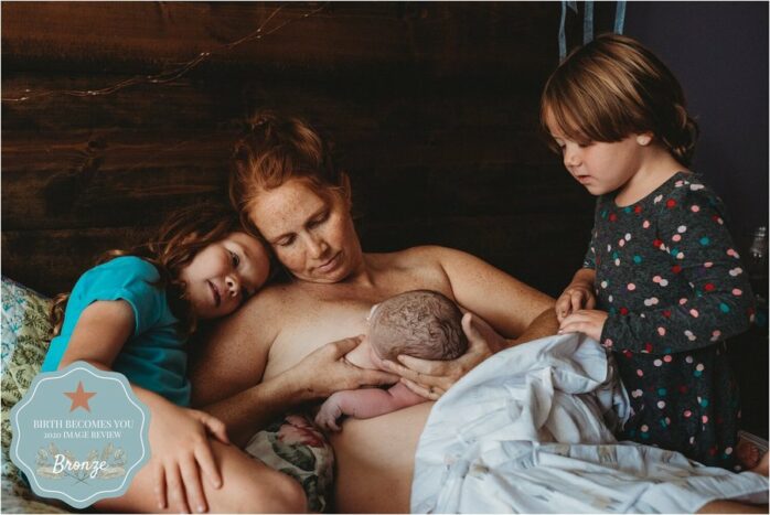 Moeder legt pasgeboren baby aan de borst terwijl haar andere twee kinderen toekijken