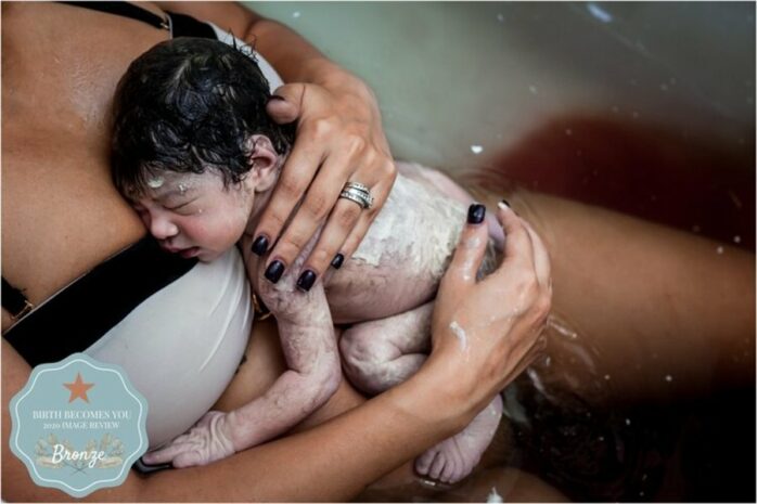 Pasgeboren baby onder de vernix ligt bij zijn moeder op de borst in bad, hij zit nog onder de donshaartjes