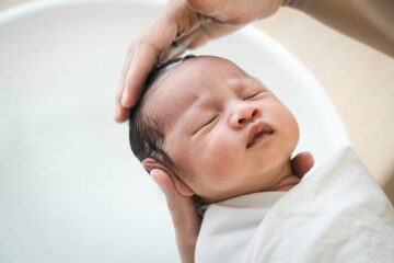 Moeder is bezig met het haar wassen van haar baby, die kalm in haar hand ligt