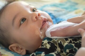 Baby die melk knoeit in zijn nekplooi waardoor een smetplek kan ontstaan