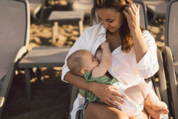 Vrouw die op het strand borstvoeding geeft aan haar baby en aan de andere kant een zoogkompres in haar bh heeft