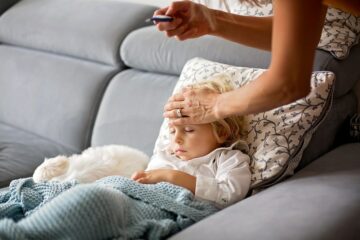 Moeder meet temperatuur van haar peuter die ligt op de bank
