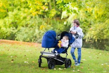 Jongetje loopt met baby's in duowagen over grasveld