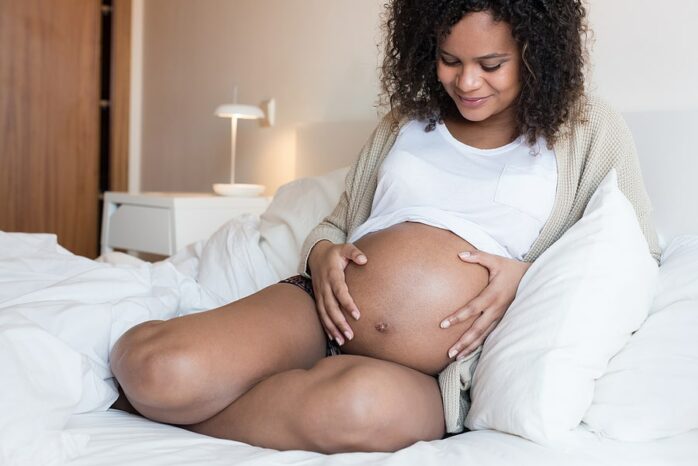 Zwangere vrouw houdt haar buik vast en kijkt liefdevol naar de zwangere buik