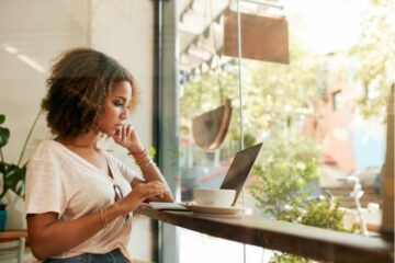 Een jonge vrouw staat in een koffietentje iets op te zoeken op haar laptop