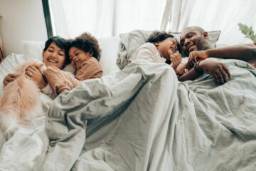 Twee ouders liggen met hun twee kinderen en hond in een familiebed.