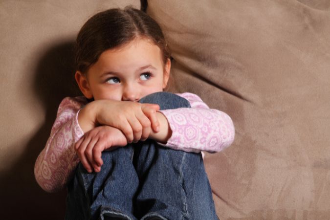 Meisje zit bang en in elkaar gedoken op de bank naar iets te luisteren