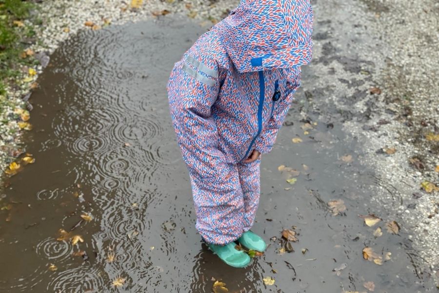 Peuter speelt in een diepe regenplas met het beste regenpak
