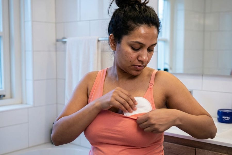 Vrouw zit op badkamer en doet zoogcompressen in haar bh