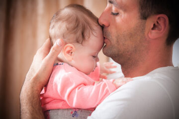 Vader houdt baby rechtop tegen zich aan om reflux te voorkomen