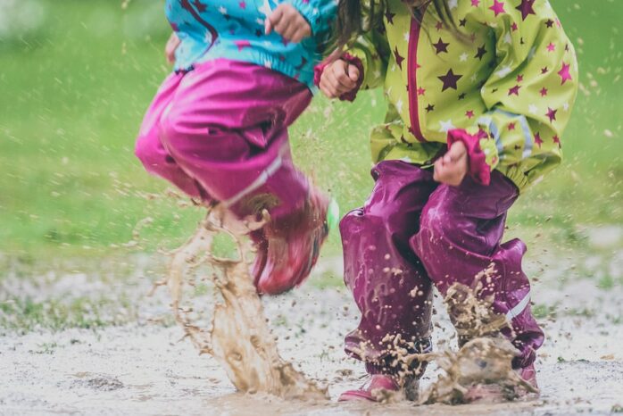Peuters zijn aan het buitenspelen en springen in regenplassen