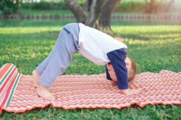 Peuter doet aan kinderyoga op een kleedje in het gras