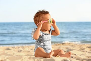 Kindje zit op het strand en draagt een babyzonnebril