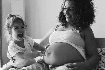 Zwangere vrouw en dochtertje kunnen baby voelen bewegen in de buik en lachen erom