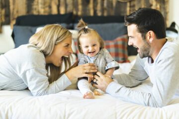 Vader en moeder kietelen baby op bed