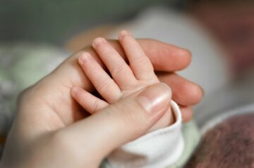 Ziek kind en relatie: ouder houdt hand van zieke baby vast en denkt erover na hoe haar zieke kindje haar relatie beinvloedt