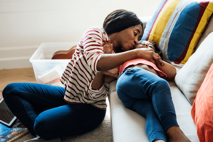 Moeder knuffelt haar dochter op de bank en is bezorgd over corona bij kinderen