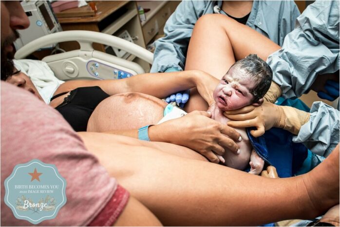 Pasgeboren baby komt uit vagina en kijkt in de camera