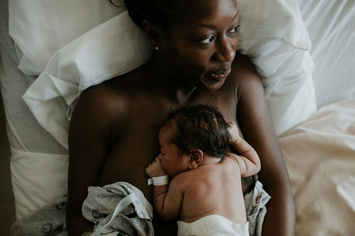 Moeder ligt met pasgeboren baby op de borst in bed