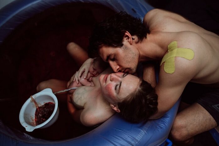 Man zoent zijn vrouw die nog in bad ligt met baby vlak na badbevalling