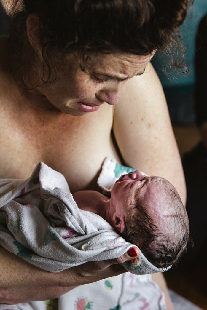 Pasbevallen vrouw kijkt haar pasgeboren baby geëmotioneerd aan