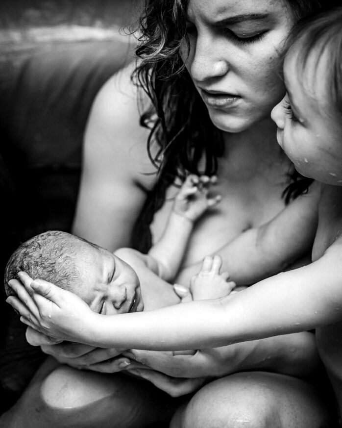 Pas bevallen moeder en haar peuterdochter houden pasgeboren baby samen vast na badbevalling