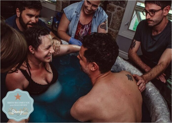 Man en vrouw zitten samen lachend in bad tijdens een badbevalling