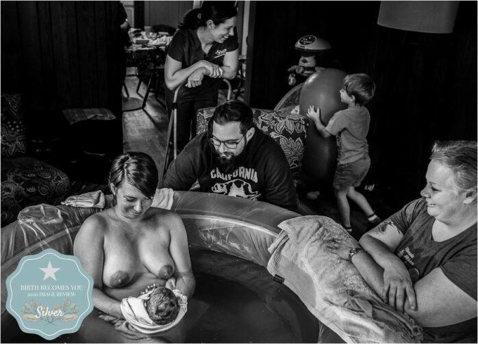 Moeder in bad bekijkt haar pasgeboren baby, vader zit aan de rand van het bad