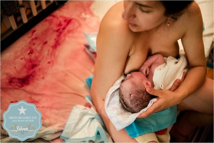 Baby ligt aan borst van pasbevallen vrouw, er is nog bloed op de lakens