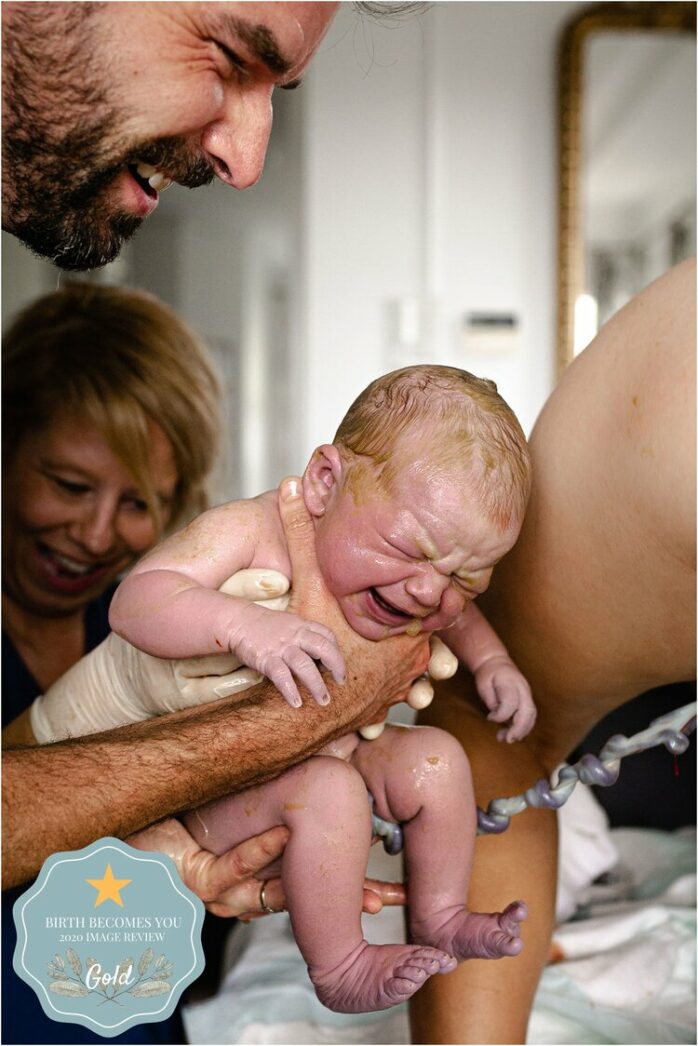 Vader houdt lachend de pasgeboren baby vast