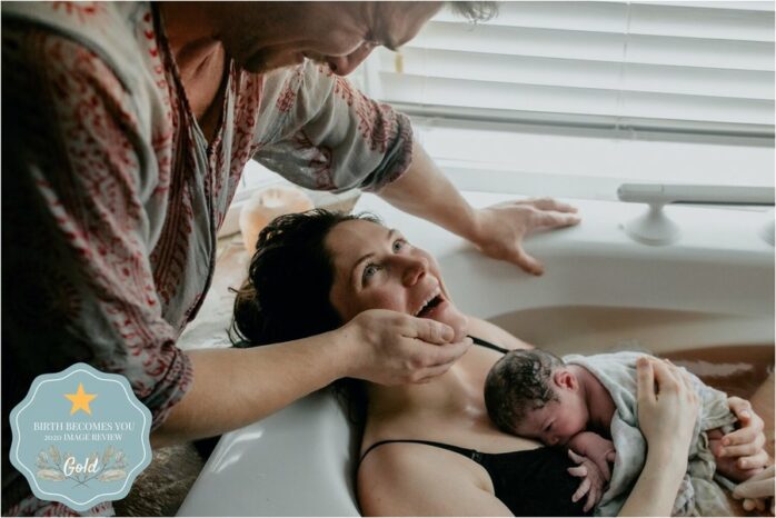 Moeder met pasgeboren baby op de borst kijkt haar partner lachend aan