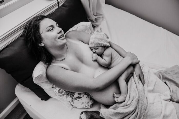 Pasbevallen vrouw ligt uitgeput maar tevreden met baby aan de borst