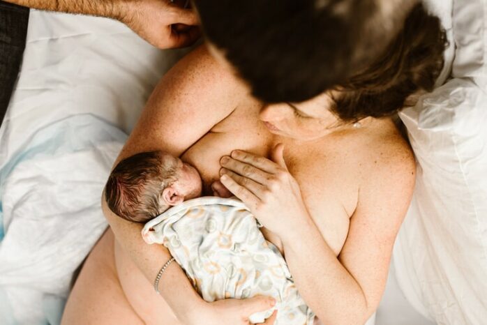 Moeder met pasgeboren baby aan de borst en partner die meekijkt