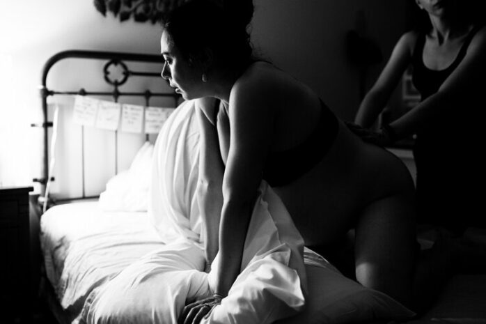 Vrouw staat voorovergebukt bij bed en vangt weeën op