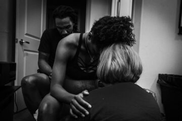 Zwangere vrouw bevalt op een baarkruk, terwijl haar partner haar ondersteunt