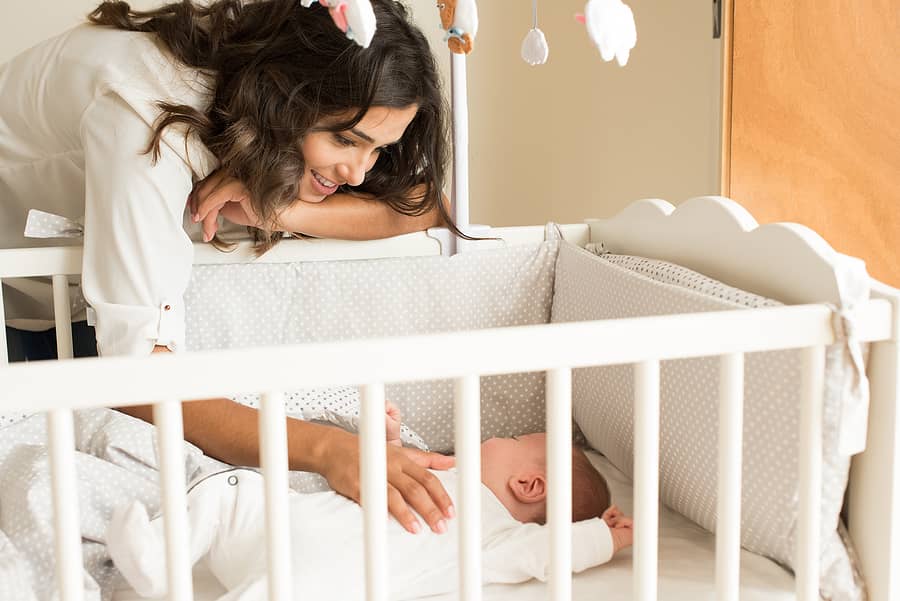 Moeder aait buik van baby in ledikant