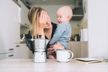 Moeder met parentale burn-out leunt op tafel met baby en koffie